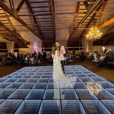 Newlyweds sharing their first dance on a white LED floor in a timber venue