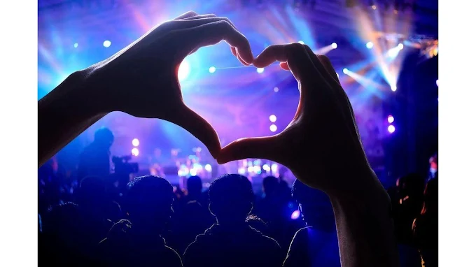 Hands forming a heart above a crowd under colourful concert lights